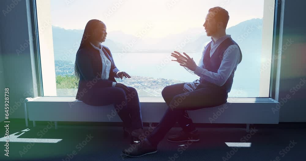 Two young business people talking together inside modern office lobby Two young business people talking together inside modern office lobby