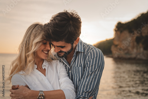 Couple in love hugging at the beach in summer. Romantic handsome man and beautiful woman standing at sea coast during the sunset.
