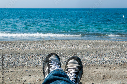 Piedi con scarpe sportive e jeans sulla spiaggia in riva al mare