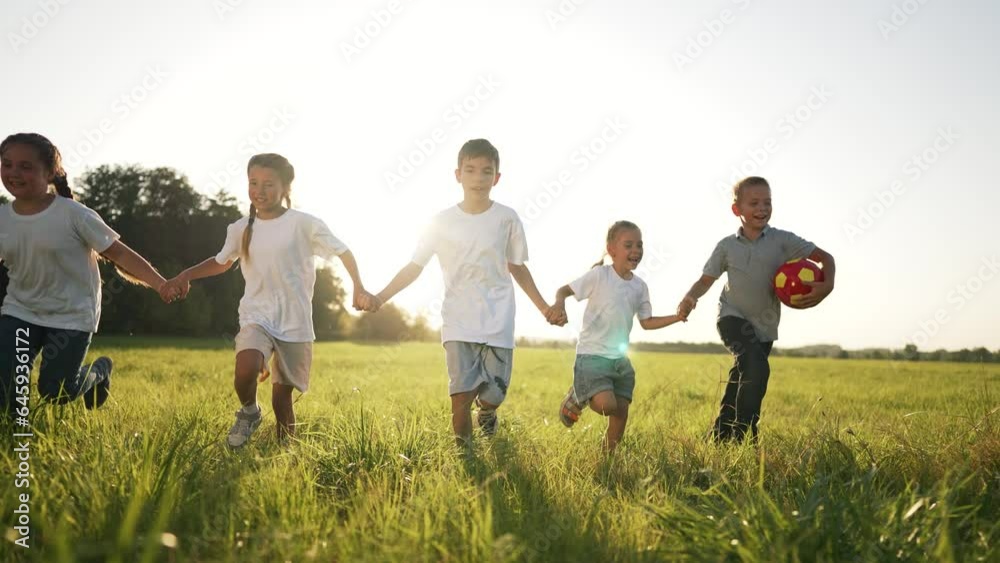 happy family.children holding hand walk run in park on green grass in summer.team of kid holding hand run with ball in nature.Kid play together as team in summer.Group of children in park in nature