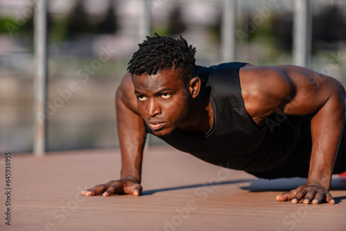 Confident young African athlete in sportswear doing push-ups while exercising outdoors