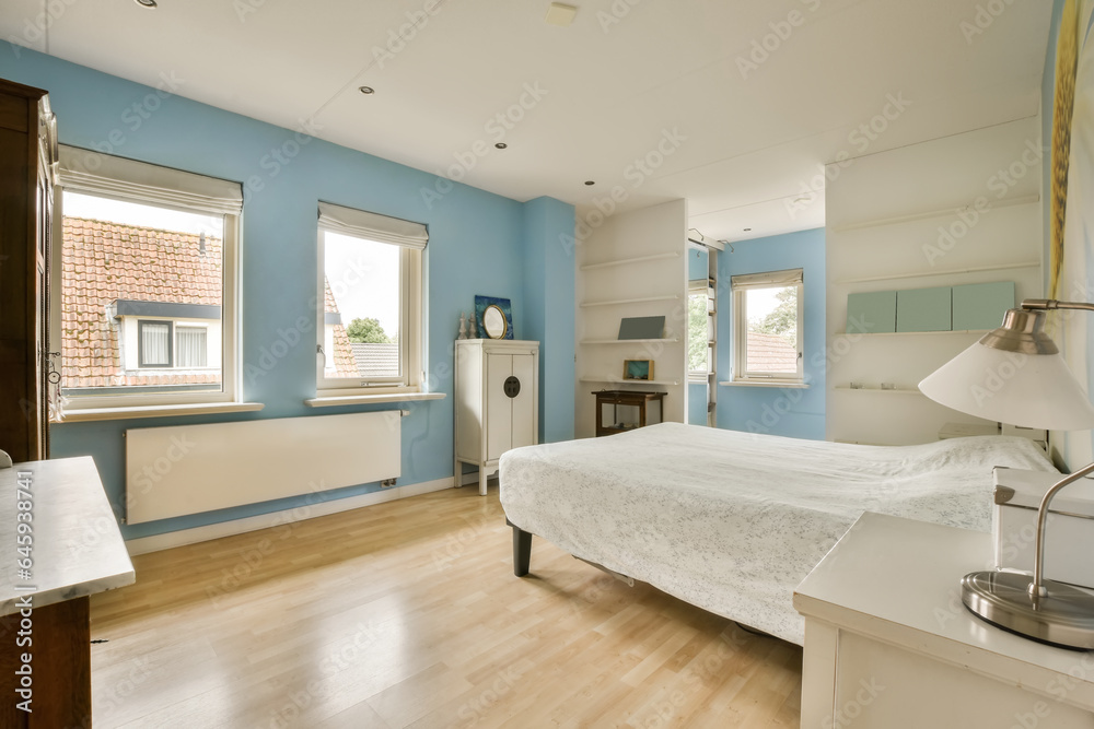 a bedroom with blue walls and wood flooring in the middle part of the room there is a white bed a bedroom with blue walls and wood flooring in the middle part of the room there is a white bed