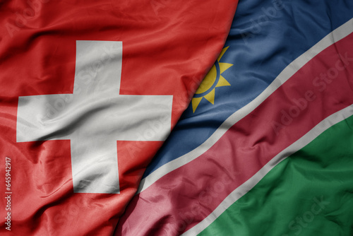 big waving national colorful flag of switzerland and national flag of namibia .