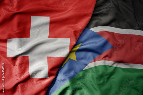 big waving national colorful flag of switzerland and national flag of south sudan