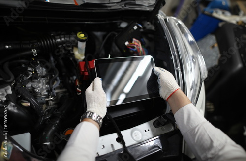Close-up of special digital tablet used for automobile checkup and fixing damaged car parts. Mechanic in white gloves and working outfit in service station. Copy space on screen. Automotive check