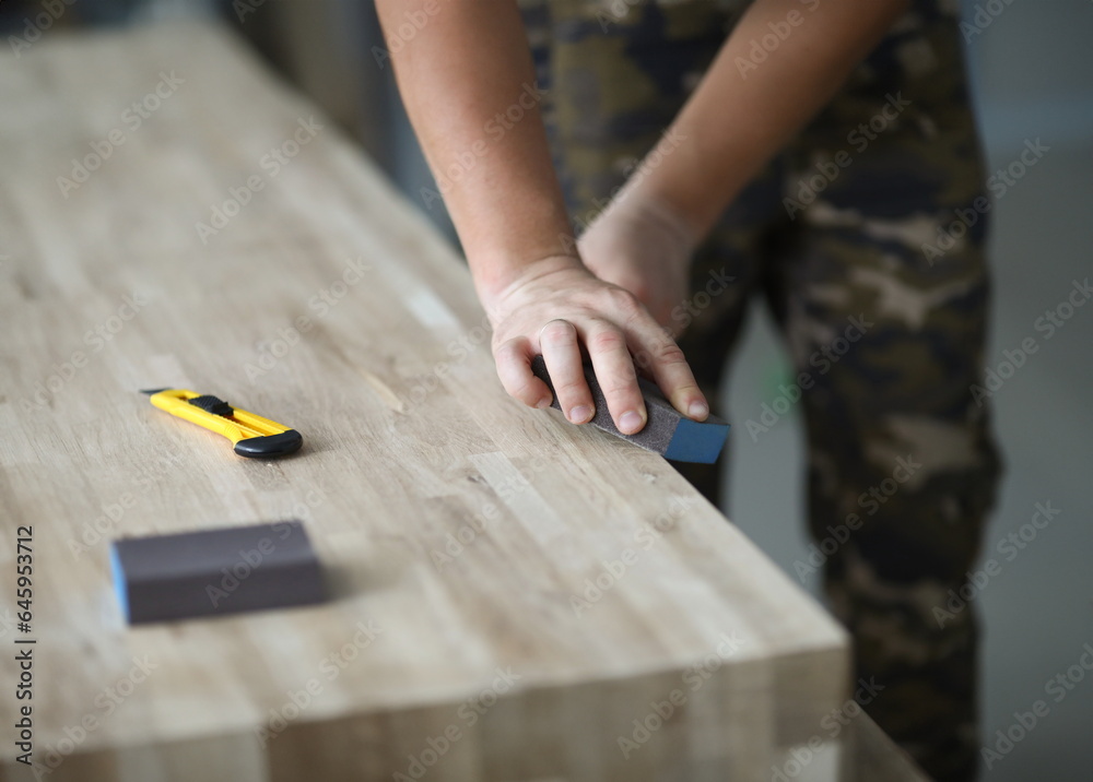 Focus on male hands holding special tool and grinding surface of desk. Manufacture of stylish wooden furniture. Carpentry workshop concept. Blurred background
