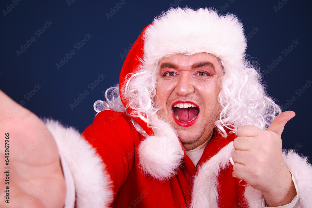 A funny drag queen enjoys life in a Santa Claus costume. Blue background.