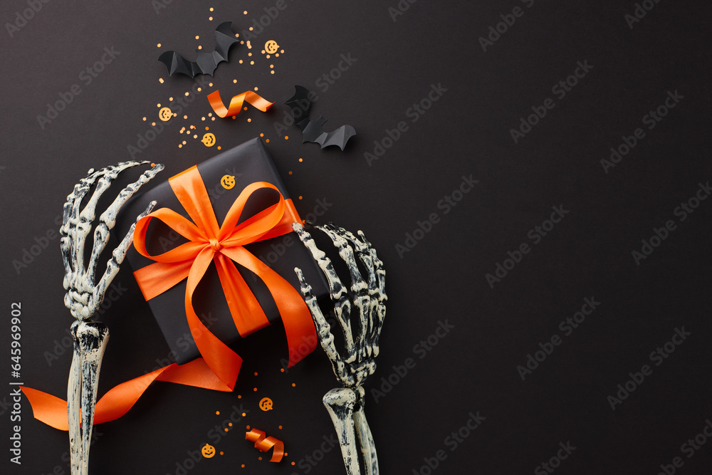 Halloween shopping extravaganza. Top view composition of skeleton hands, satin ribbon bows, black presents, spooky insects, confetti on black background with advert space