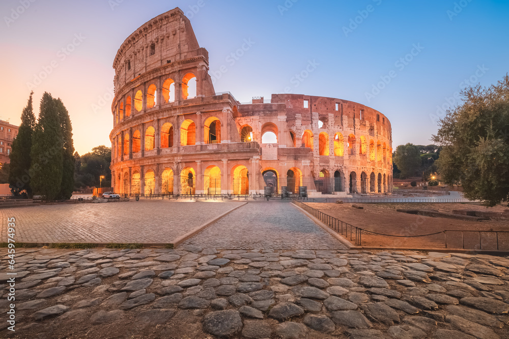 Iconic Flavian Amphitheatre, the ancient Roman Colosseum, a famous tourist landmark illuminated at twilight and dawn in historic Rome, Italy.