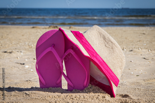 Straw hat and slippers on sand at beach. Accessories for relax in summer