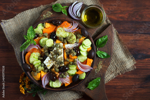 Classic Greek salad with yellow tomatoes, cucumbers, olives, capers and soft cheese on a dark wooden surface