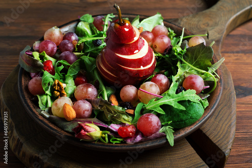 Bright and tasty salad with red pear, grapes, arugula, nuts and dried fruits on a brown plate