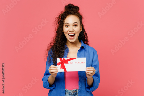 Young fun woman of African American ethnicity she wear blue shirt casual clothes hold gift certificate coupon voucher card for store isolated on plain pastel pink background studio. Lifestyle concept.