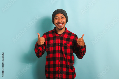 Confident Young Asian man showing a thumbs-up gesture, isolated on a blue background photo