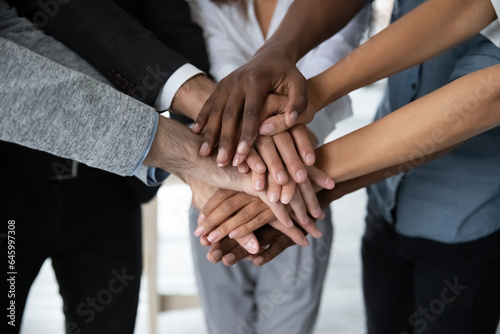 Close up of multiracial colleagues stack hands in pile engaged in teambuilding activity in office together, motivated diverse coworkers have business training at meeting, show unity, teamwork concept