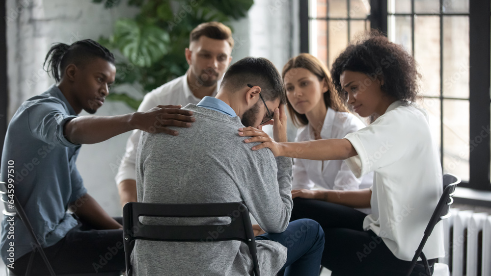 Diverse people sit in circle participate in group psychological session, touch support upset friend, multiracial colleagues comfort unhappy stressed male suffering from mental addiction problems Diverse people sit in circle participate in group psychological session, touch support upset friend, multiracial colleagues comfort unhappy stressed male suffering from mental addiction problems