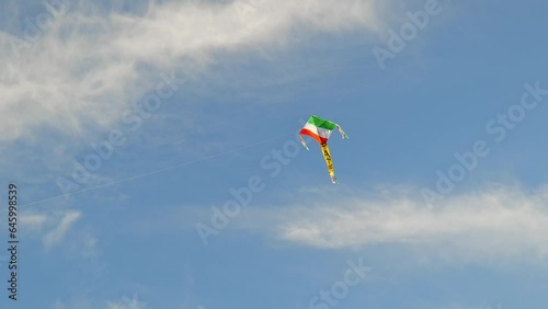 A kite with the colors of the Italian flag flies in the blue sky, in Turin along the Po river. On its tail there is the inscription PACE in Italian. Slow motion video.