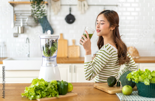 Portrait of beauty healthy asian woman making green vegetables detox cleanse and green fruit smoothie with blender.young girl drinking glass of smoothie, fiber, chlorophyll in kitchen.Diet, healthy