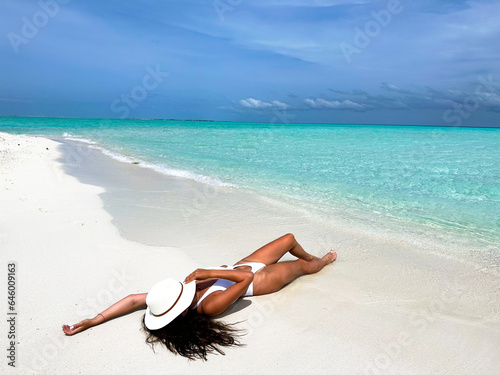 Canvas Print A sexy tanned girl, dressed in a white bikini, reclines sensuously on the white sands of the beach