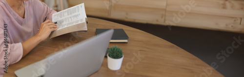 Female entrepreneur working at home to reading a book and searching business data on laptop