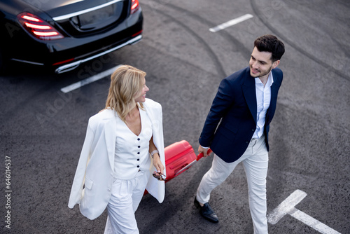 Business couple walking with a suitcase on parking lot, arrived by luxury taxi, view from above. Concept of transportation and business trips