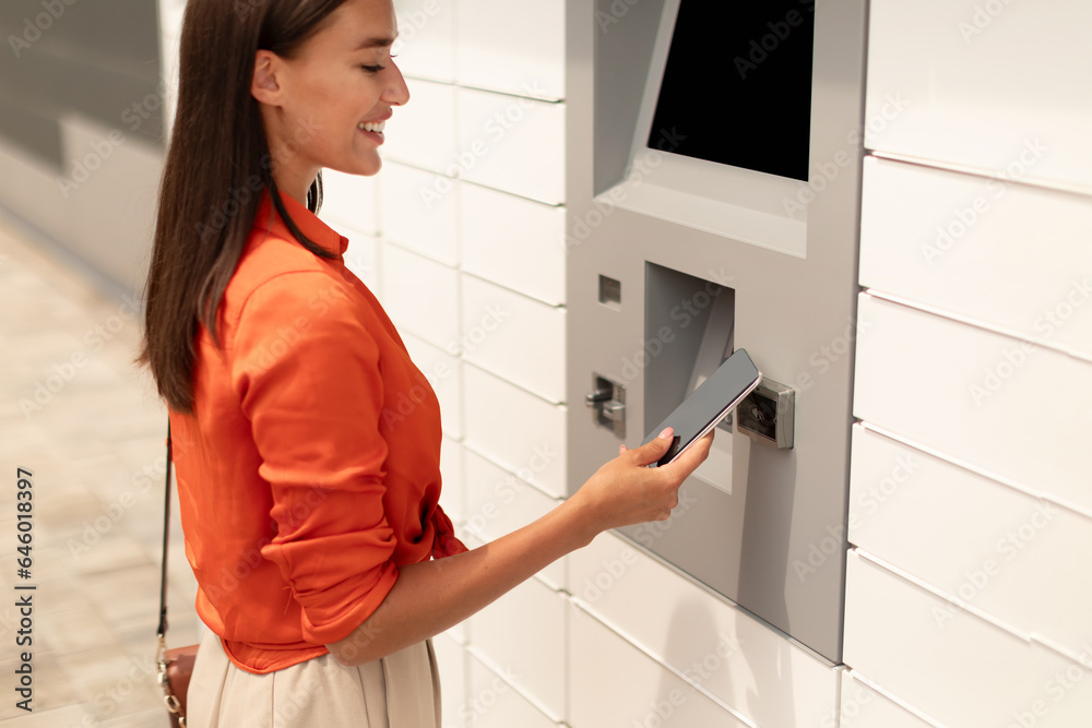 Young Woman Withdrawing Money At Atm Using Phone In City Young Woman Withdrawing Money At Atm Using Phone In City