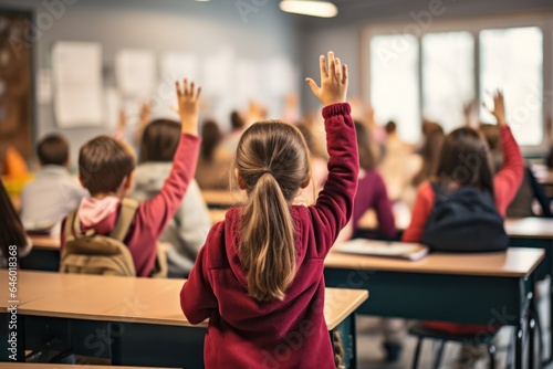 Back view of little girl raising her hands in the classroom at school