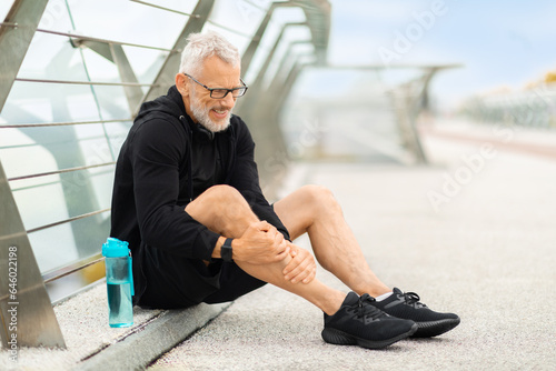 Foto Elderly sportsman jogging by bridge, suffering from shin splint
