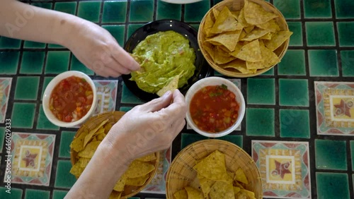 Family hands eating Mexican food corn nachos dipping salsa and avocado guacamole sauce