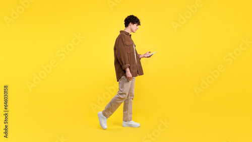 Sad guy using cell phone while walking over yellow background