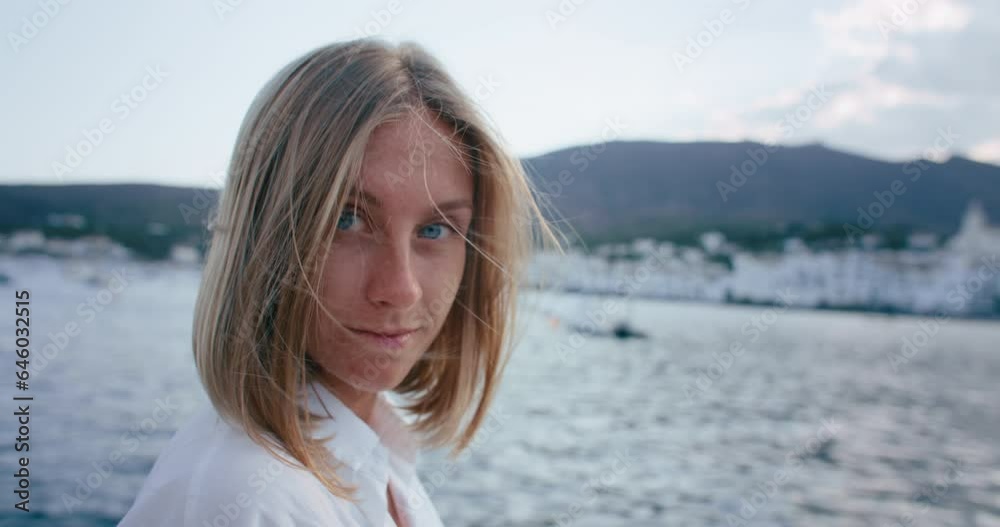 Portrait of young woman peacefully looking at the camera. Female tourist enjoy summer vacation, smile and lough. Light breeze in her hair. Beach town on the background. Portrait of young woman peacefully looking at the camera. Female tourist enjoy summer vacation, smile and lough. Light breeze in her hair. Beach town on the background.