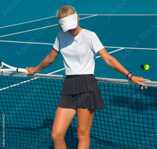 girl tennis player stands leaning on the tennis net on the court on a bright sunny day © Павел Мещеряков