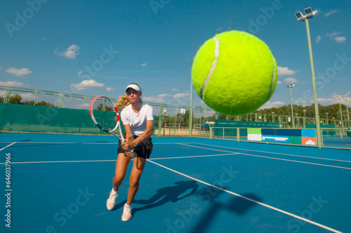 A girl plays tennis on a court with a hard blue surface on a summer sunny day. focus on tennis ball 