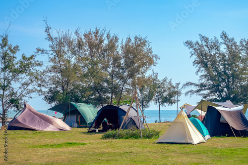 Camping tent and activity on field near the beach. Tent camping area for tourists on lawn near the beach. Holiday outdoor activities with travel and camping at seaside. Happiness outdoor recreation. © JinnaritT