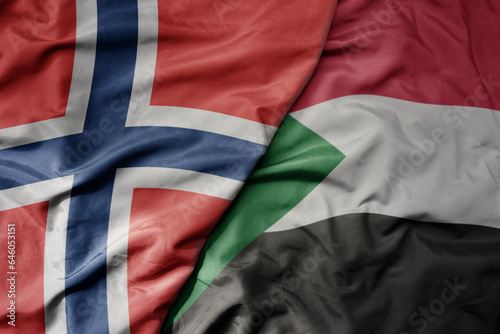 big waving national colorful flag of norway and national flag of sudan .