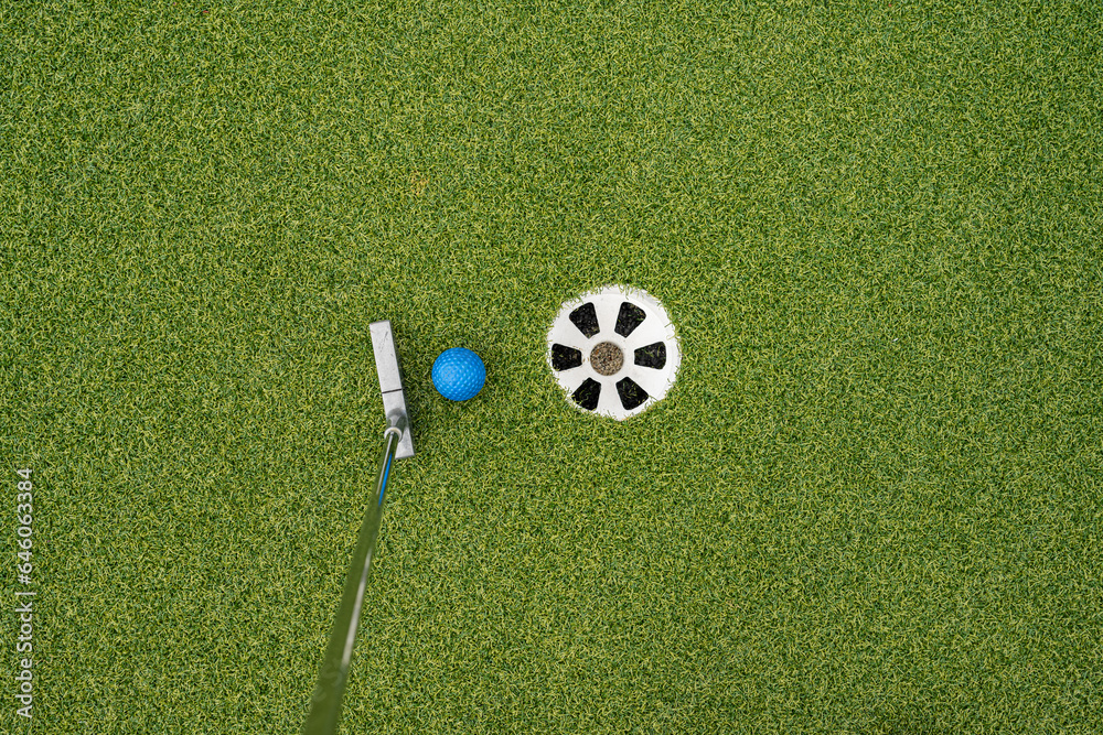 Obraz premium Miniature golf putter by blue ball and hole.