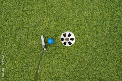 Miniature golf putter by blue ball and hole.