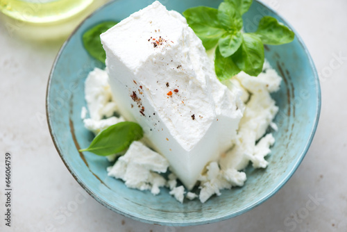 Block of feta cheese and fresh green basil in a turquoise bowl, middle close-up, selective focus