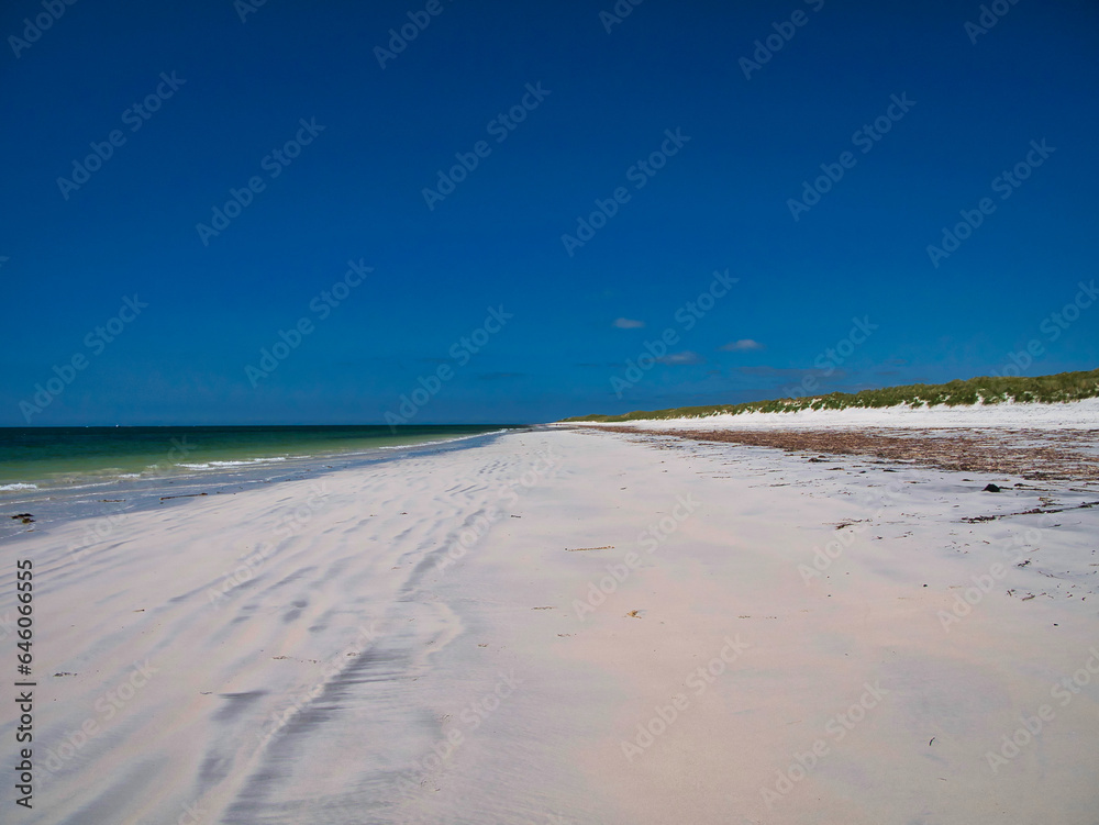 Windswept white sand between the sea and the machair on a deserted beach on the island of South Uist in the Outer Hebrides, Scotland, UK. Taken on a clear sunny day in summer with a cloudless blue sky