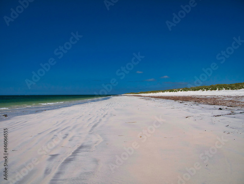 Windswept white sand between the sea and the machair on a deserted beach on the island of South Uist in the Outer Hebrides, Scotland, UK. Taken on a clear sunny day in summer with a cloudless blue sky