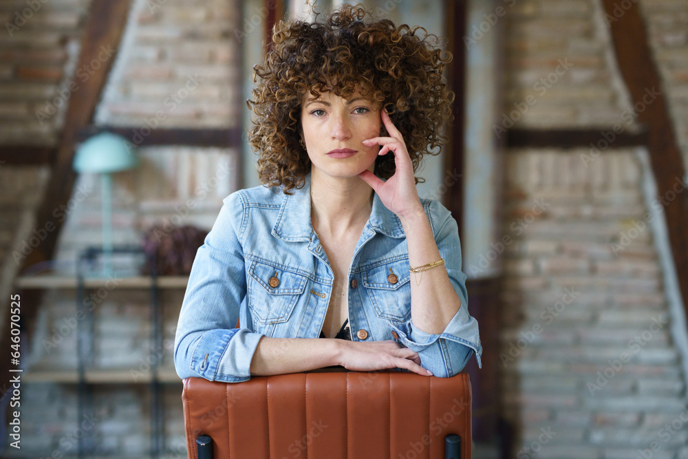 Fototapeta premium Serious young woman wearing denim jacket sitting on leather chair