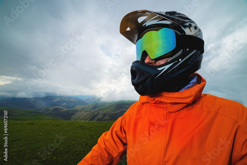 Portrait of a cyclist in a full-face helmet and sunglasses on the background of a mountain. Sport, motocross and portrait of a man in a helmet for off-road racing, mountain biking and training © yanik88