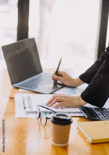 Asian Businesswoman Using laptop computer and working at office with calculator document on desk, doing planning analyzing the financial report, business plan investment, finance analysis concept.