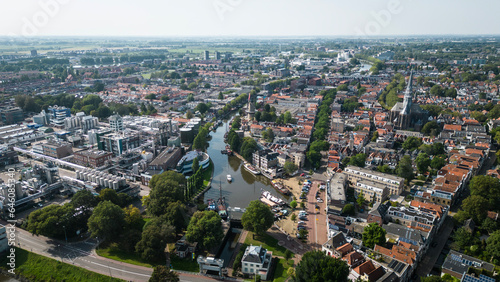 Aerial drone shot of treetops, trees, houses and shop rooftops of Dutch city Gouda centre with historic building het Tolhuis or toll house with nieuwe veerstal road on clear sunny day © drew