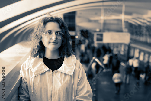 Portrait of a beautiful young woman with long curly hair in a white jacket and glasses on the background of the subway station