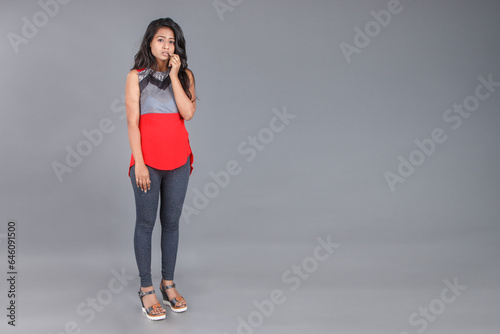 Studio shot of a young, beautiful Indian female model in casual wear wearing red and grey designer top and blue jeans against grey background. Female model. Fashion Portrait. © Anupam