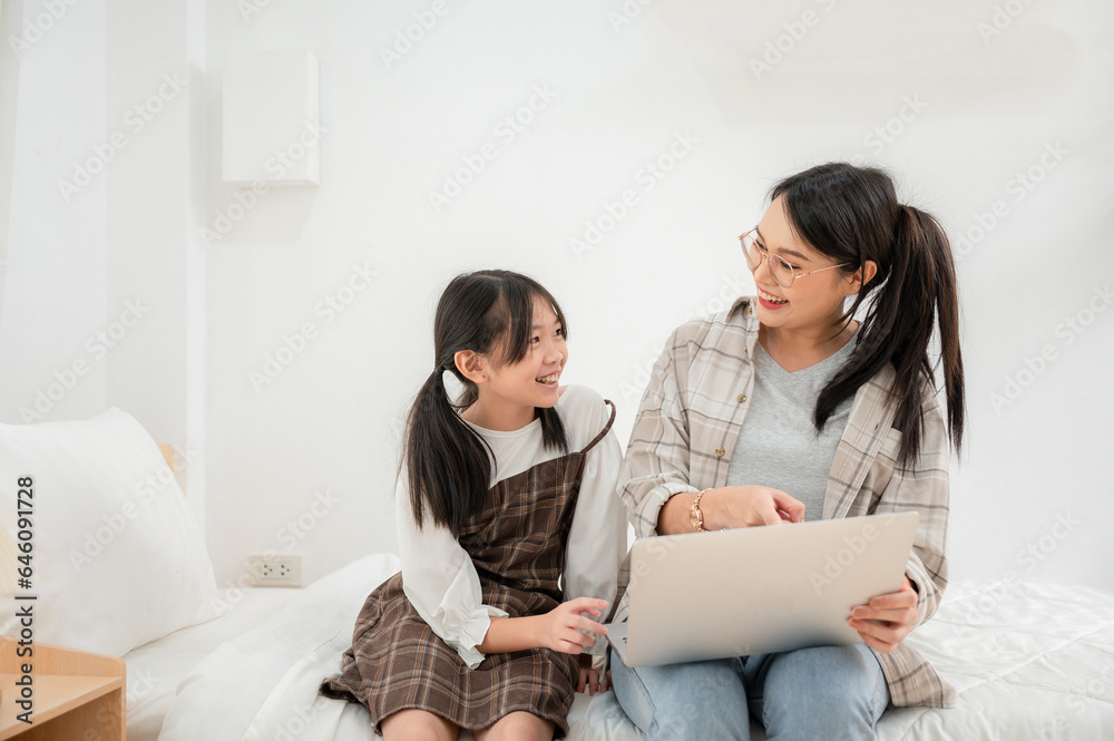 Portrait of smiling mother helping daughter with homework at home using a laptop computer Mother helping daughter with homework at home living room Portrait of smiling mother helping daughter with homework at home using a laptop computer Mother helping daughter with homework at home living room