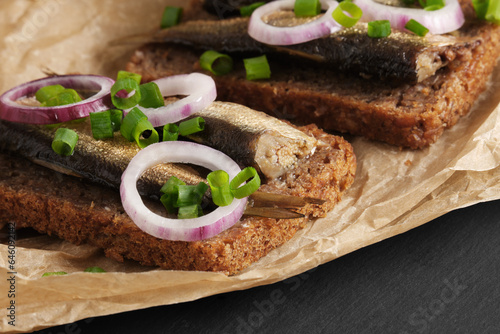 Fotografie Sandwiches with sprats, red and green onions on baking paper on black stone background