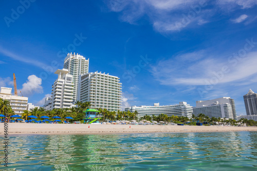 Beautiful view of white sandy beach Atlantic Ocean with sun loungers, sun umbrellas on backdrop of buildings. Miami Beach. USA. 