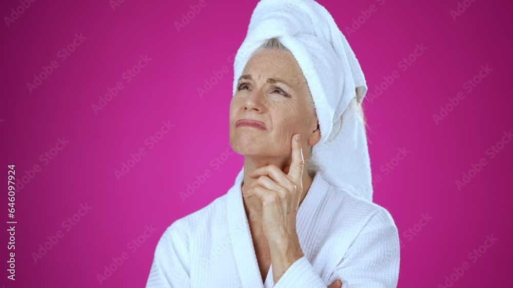 Attractive mature woman 50s, 60s, wearing bathrobe, looks at camera gives mind blown gesture showing explosion of ideas posing on solid pink background with copy space.